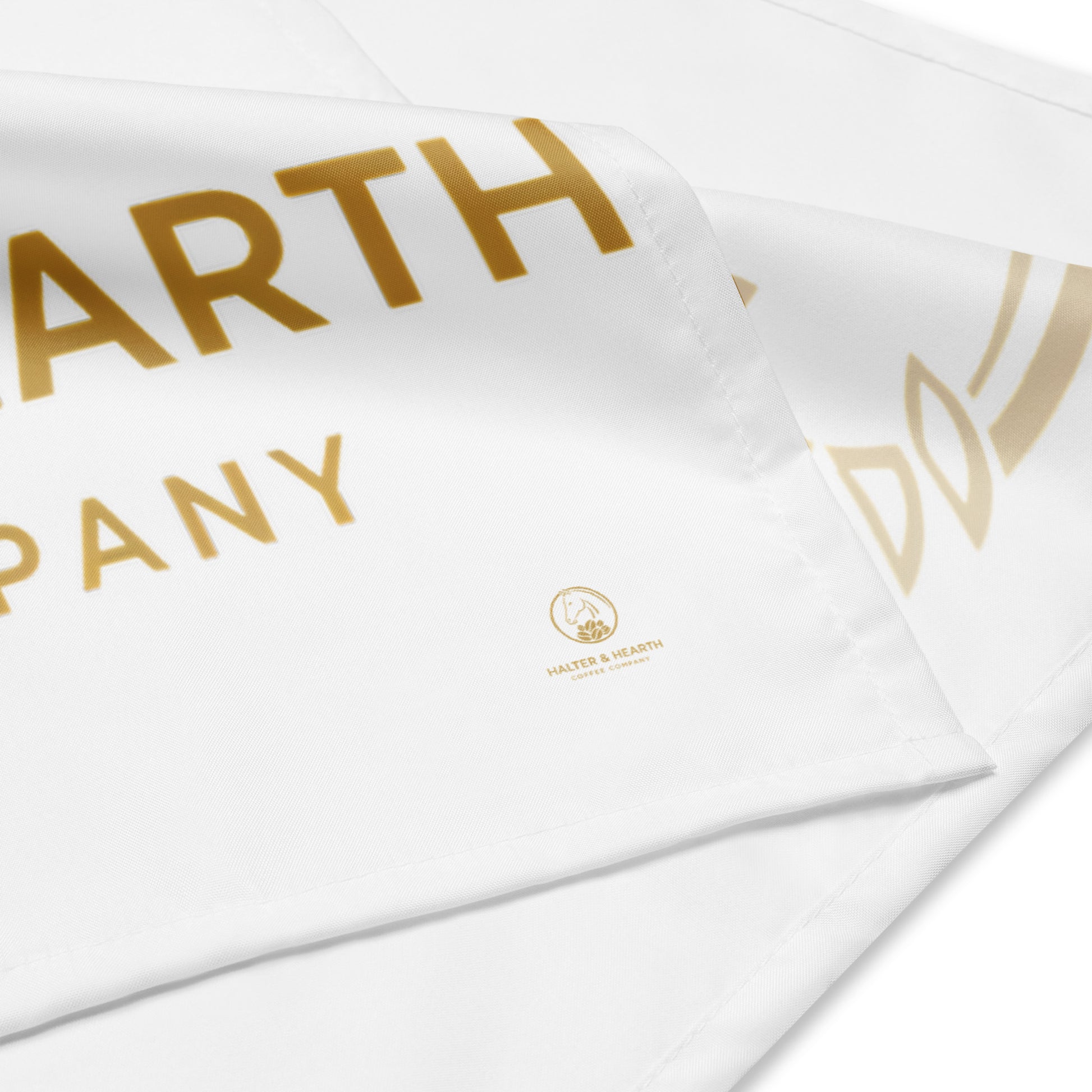 The corner of a white bandana with gold letters and the gold Halter & Hearth logo on a white background.